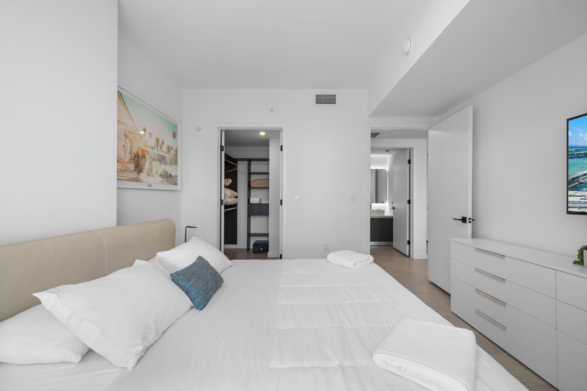 Une chambre d’hôtel moderne dotée d’un grand lit, d’un dressing et d’une salle de bain visible à travers une porte ouverte.