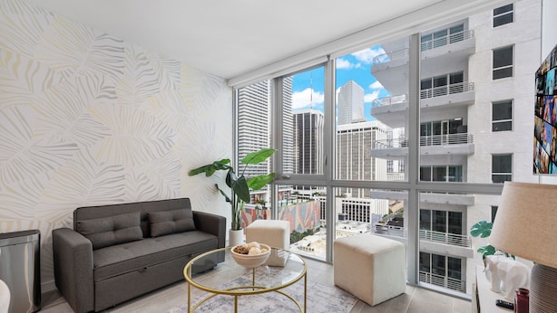 A modern living room with a grey sofa, a round coffee table, and a large window offering a city view.