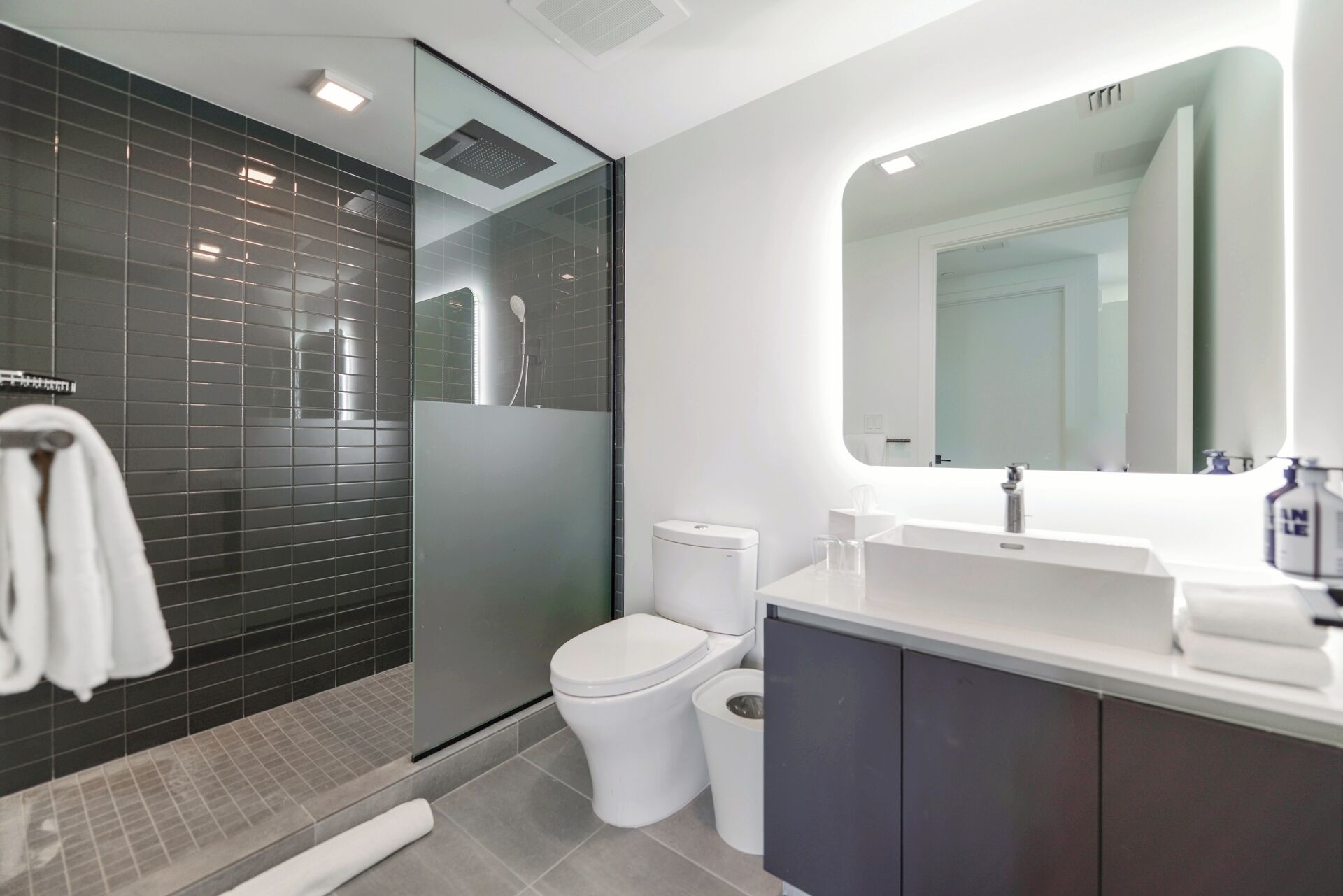 A modern bathroom with a glass-enclosed shower, a white toilet, and a vanity with a mirror.