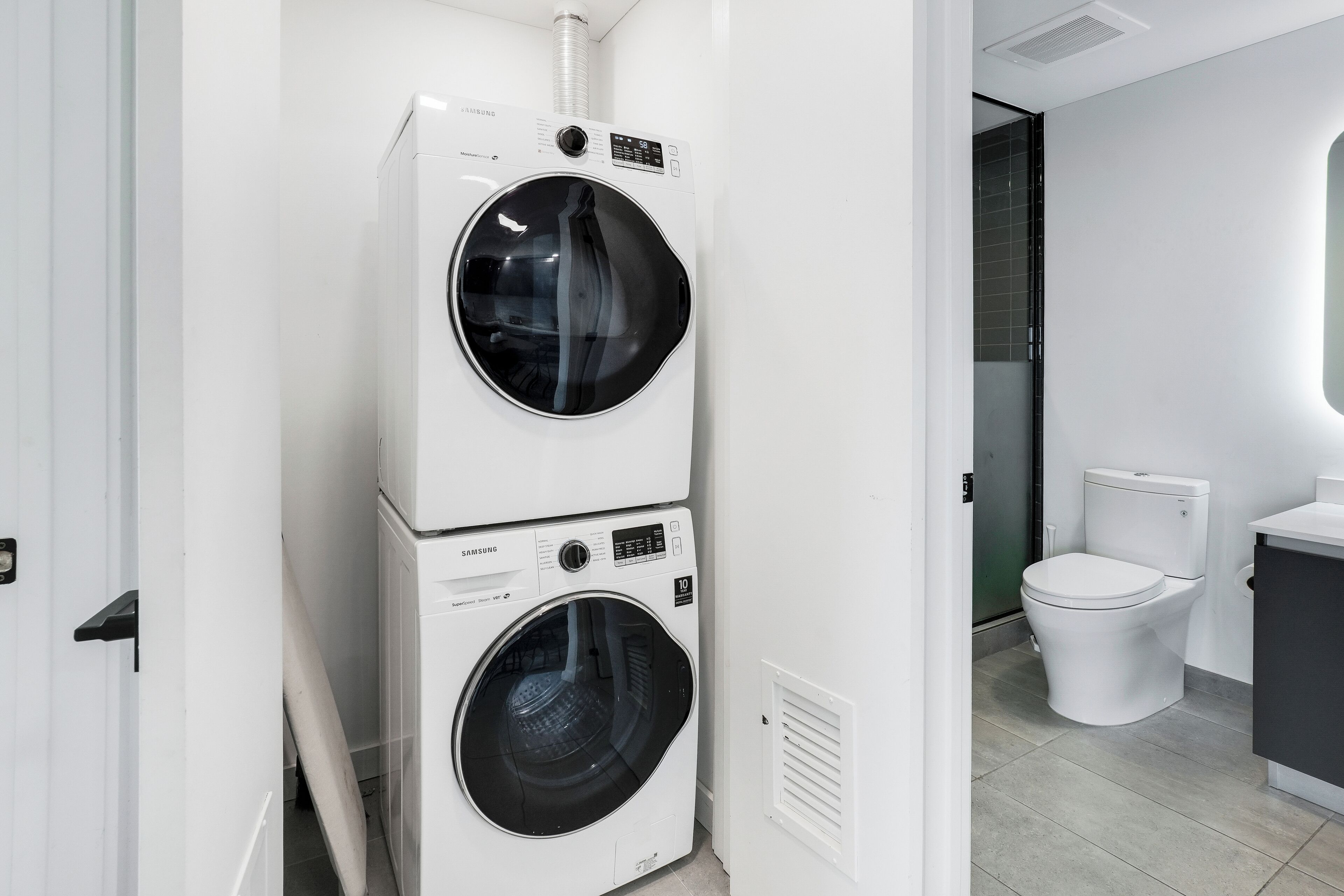 A modern laundry room with two stacked front-loading washing machines and a toilet.