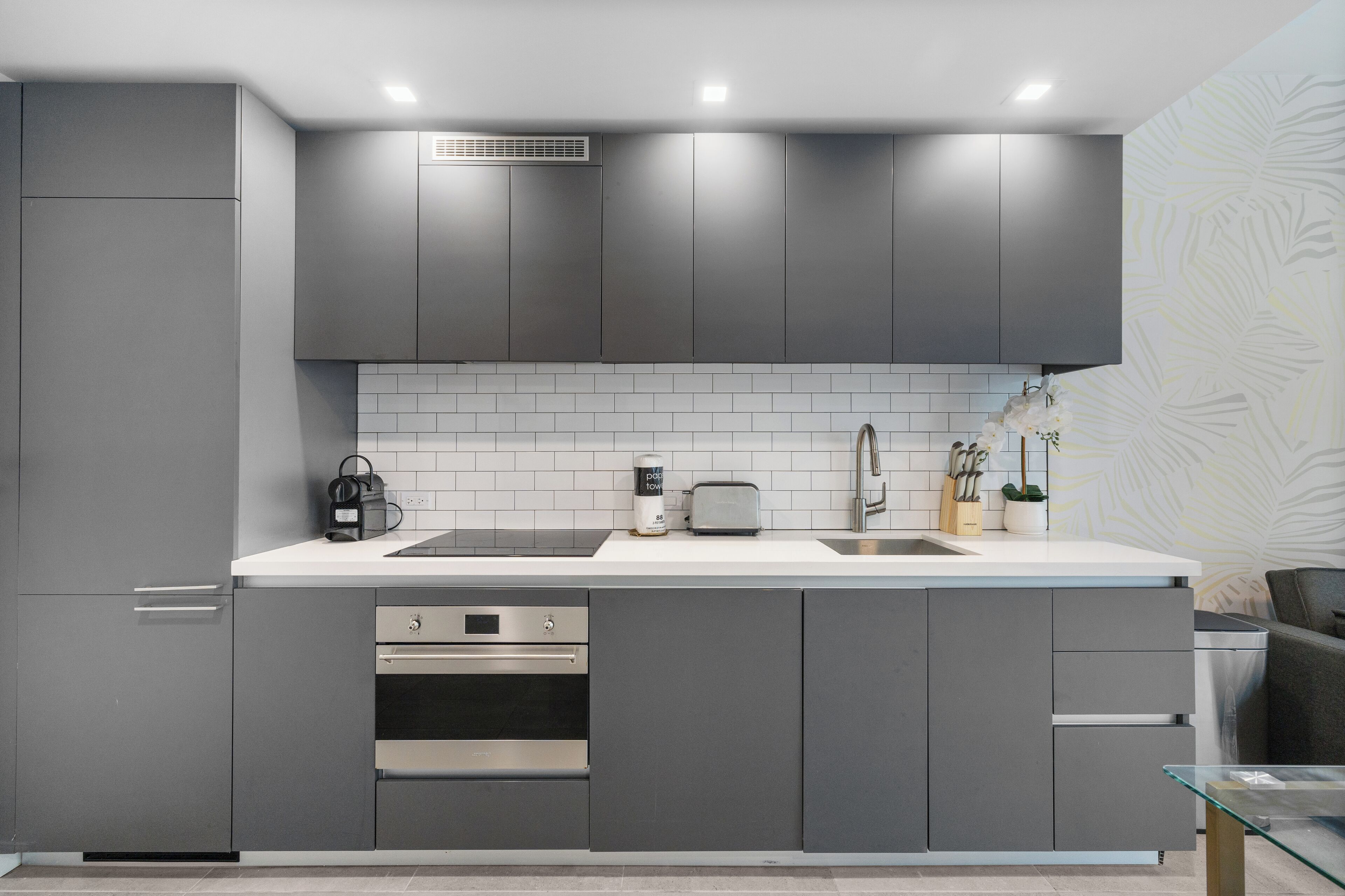 Una cocina moderna con gabinetes grises, encimera blanca, horno empotrado y pileta.