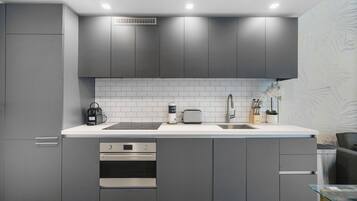 Una cocina moderna con gabinetes grises, encimera blanca, horno empotrado y pileta.