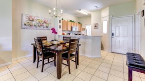 A dining area with a wooden table and chairs, a chandelier, and a painting of flowers on the wall.