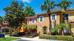 A row of colorful townhouses with palm trees, a clear blue sky, and a visible address sign.