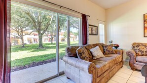 A living room with a large sliding glass door leading to a grassy outdoor area, a brown leather sofa, and a patterned armchair.
