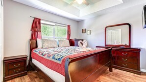 Une chambre à coucher avec un lit en bois, une table de chevet, une commode, un miroir et une fenêtre avec des rideaux.