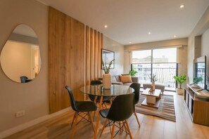 A modern living room with a glass dining table, black chairs, a sofa, and a TV. - Capac by Wynwood House (Lima)