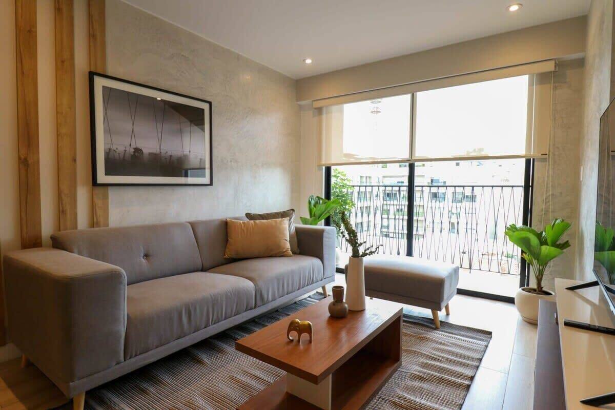 A modern living room with a grey sofa, a wooden coffee table, and a large window with a balcony view.