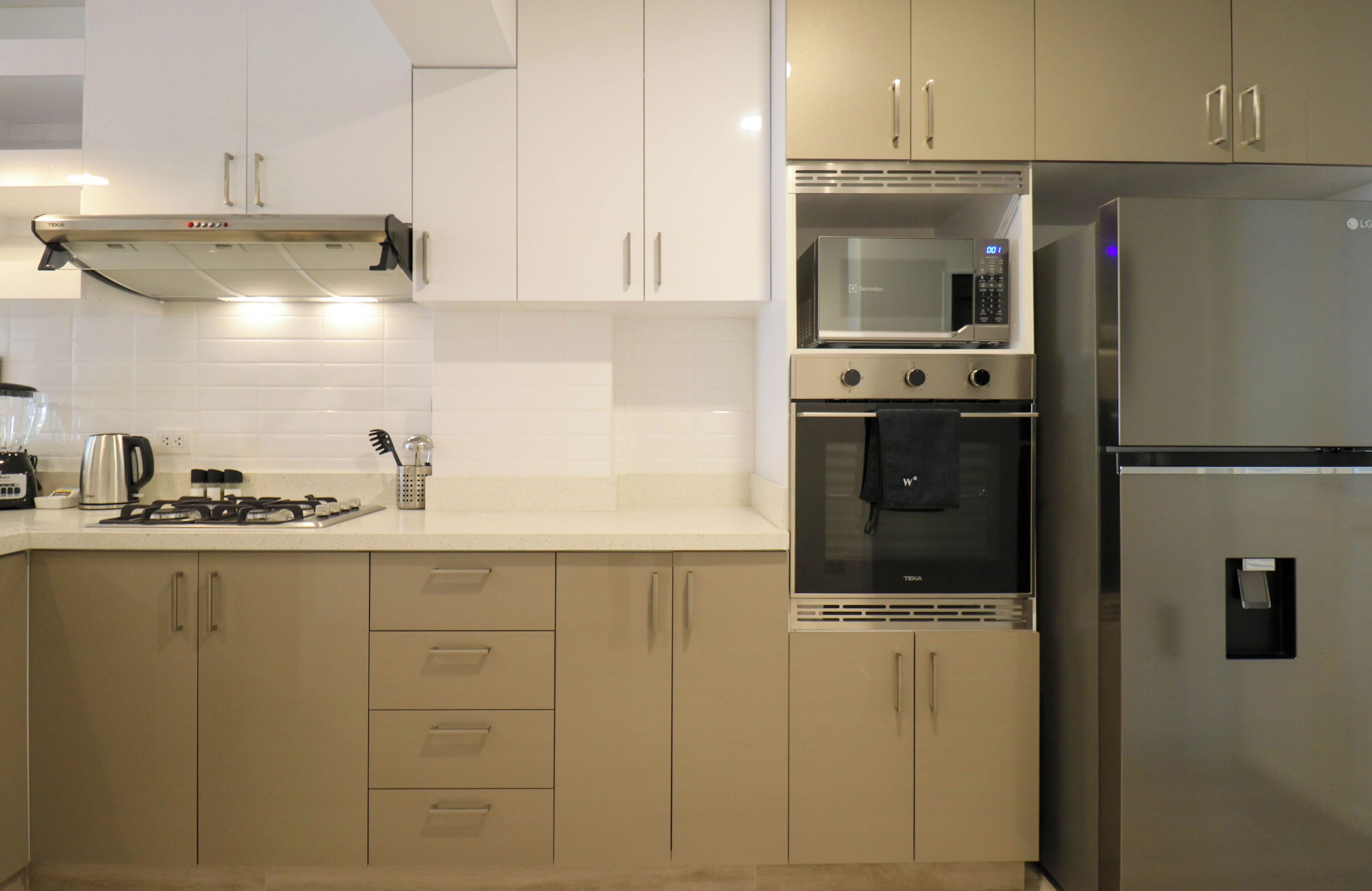 A modern kitchen with beige cabinets, a stainless steel refrigerator, a microwave, and an oven.