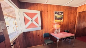 A room with wooden walls, a table with chairs, a lamp, and a framed picture on the wall. - Room 6 • Retro Desert Escape  - Joshua Tree (Joshua Tree)