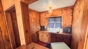 A wooden cabin interior with a kitchen area, including wooden cabinets, a sink, a toaster, and a refrigerator. - Room 6 • Retro Desert Escape  - Joshua Tree (Joshua Tree)