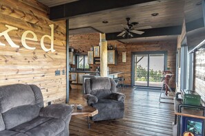 Amplia sala de estar con pared de madera, un sillón gris, una mesa de centro de madera y un ventilador de techo.