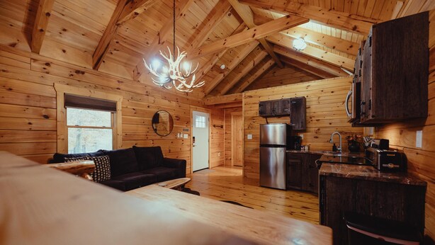 Interior de una cabaña de madera con comedor, cocina y techo con vigas a la vista.