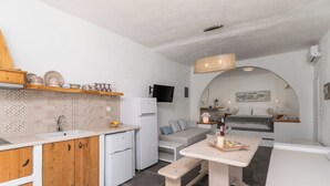Een kleine keuken met houten kastjes, een witte koelkast en een eethoek met een bank.