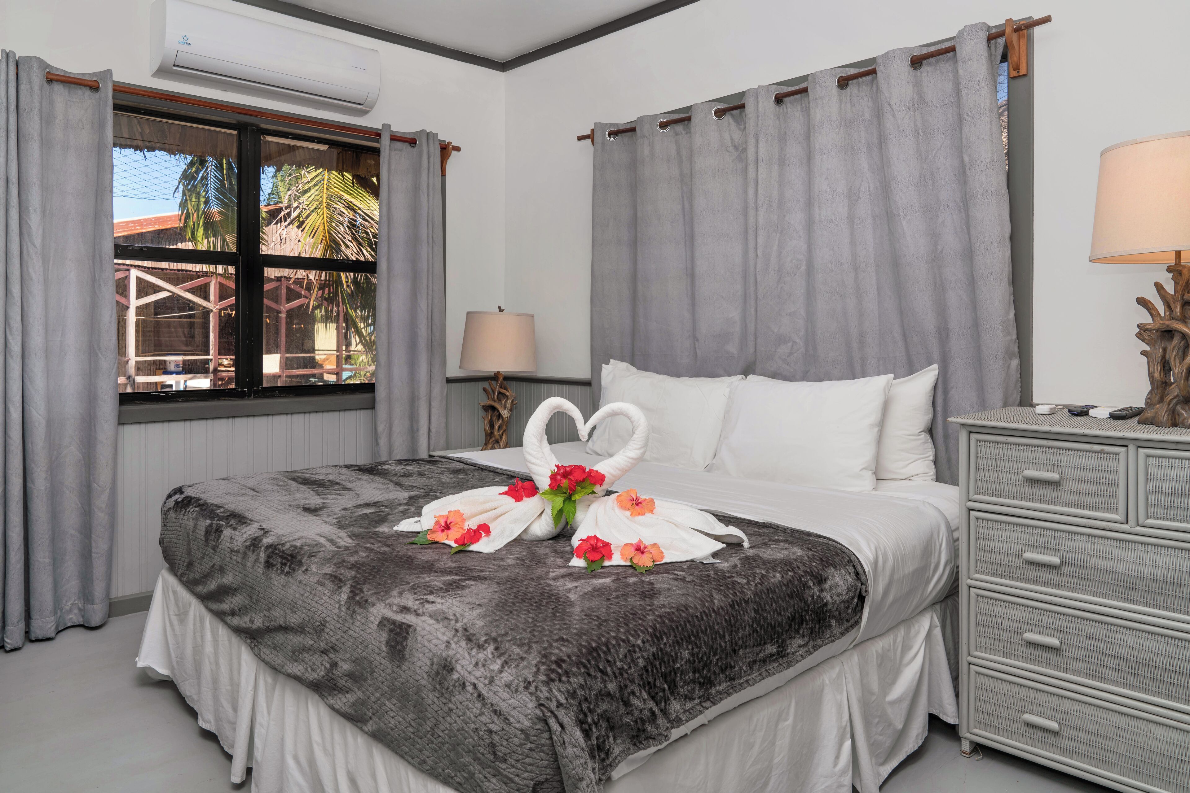 A neatly made bed with a gray blanket, a decorative swan centerpiece, and a dresser with drawers.