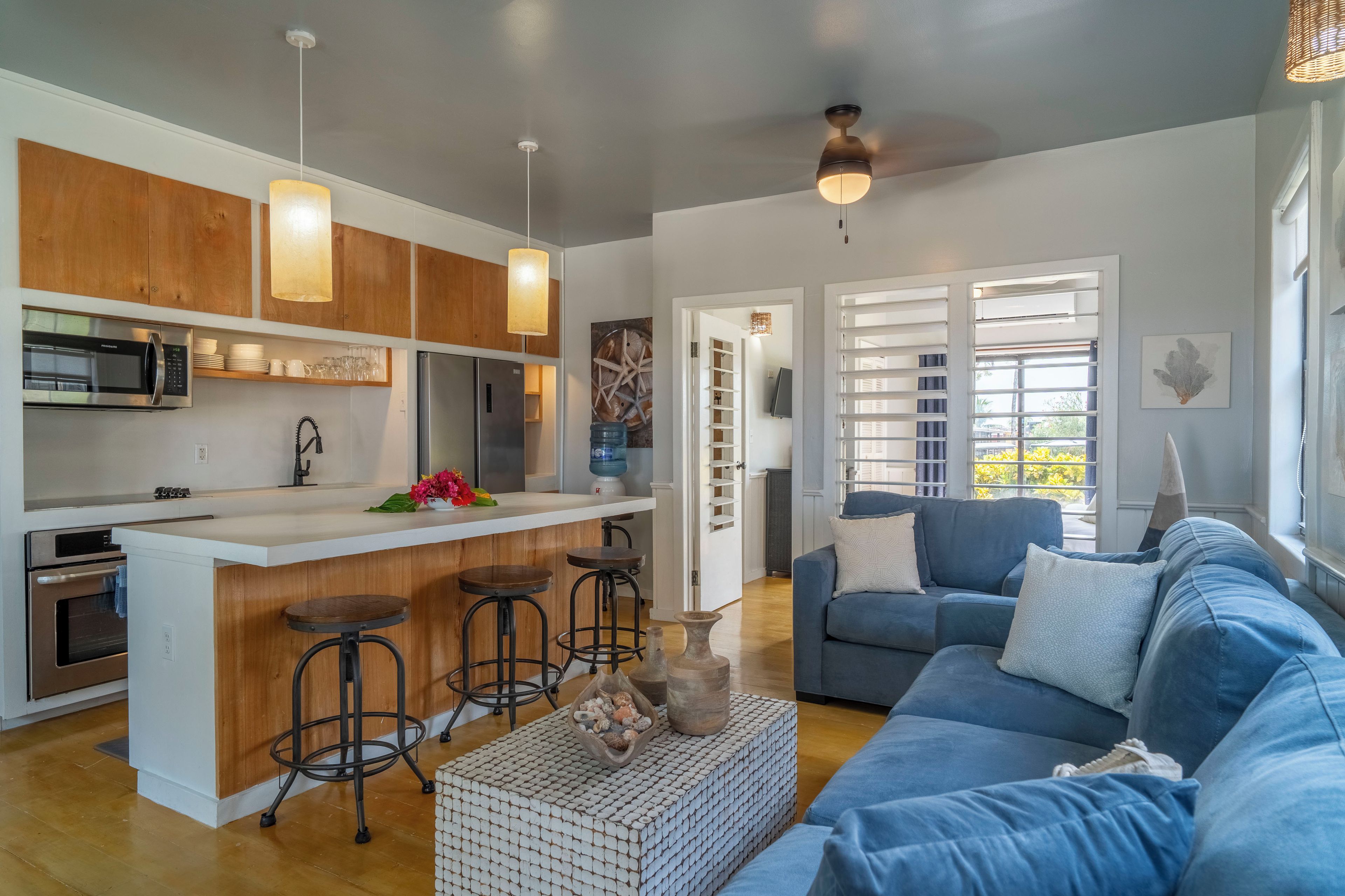 A modern kitchen with a central island, bar stools, and a dining area with a blue sofa and a coffee table.
