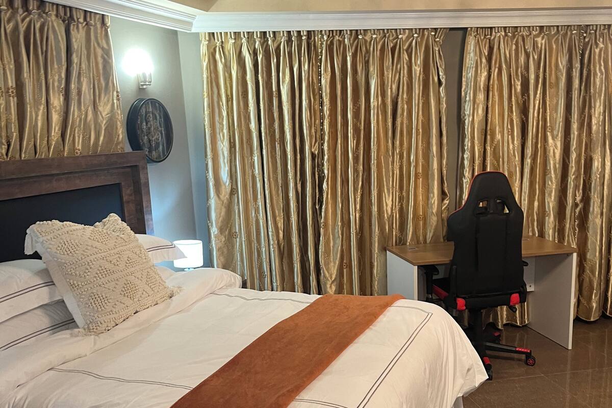 A hotel room with a large bed, a desk, a chair, and curtains.