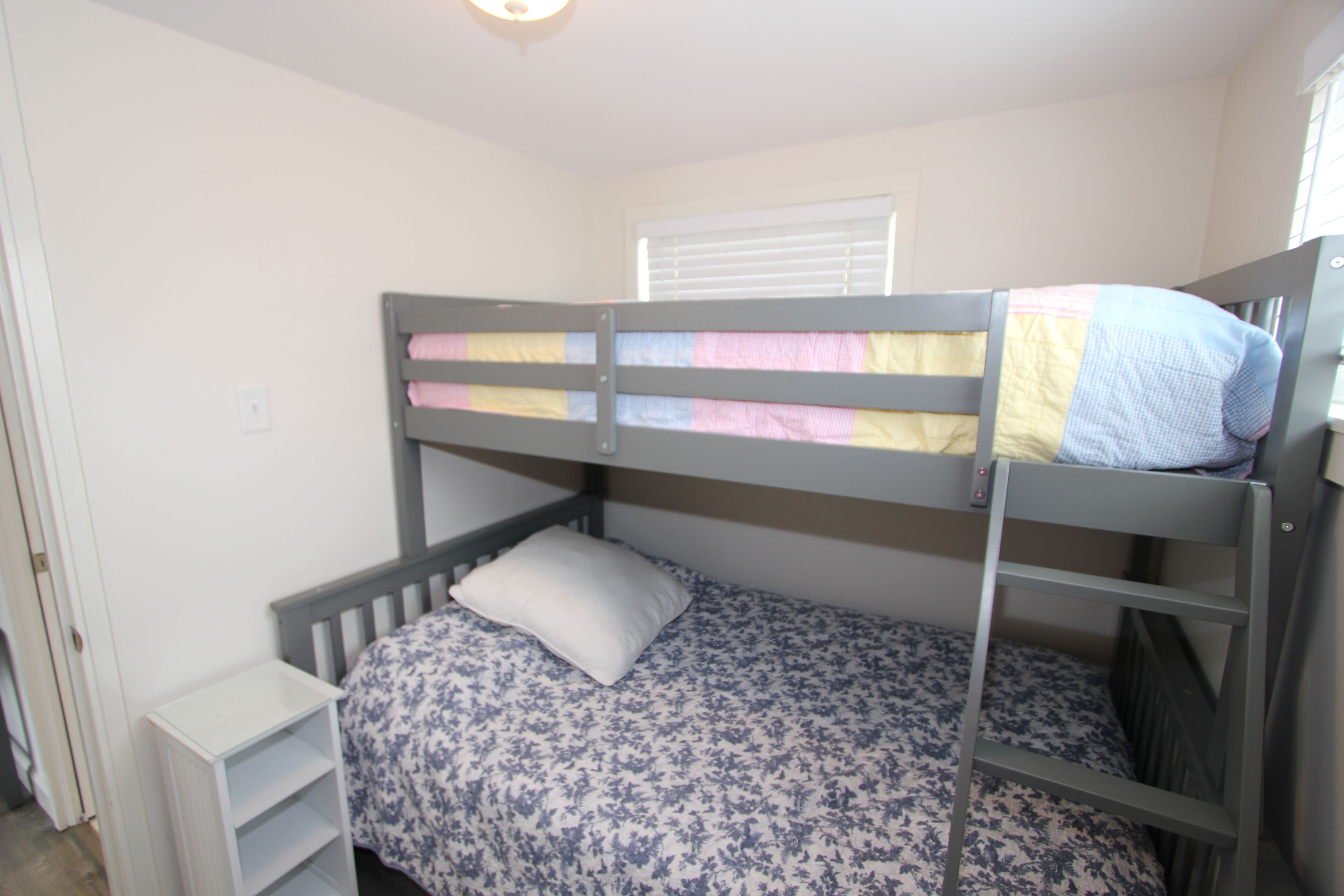A bunk bed with a floral bedspread, a white pillow, and a small white nightstand.