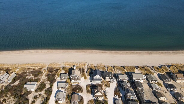 Vista aérea de una zona residencial costera con casas dispuestas en filas a lo largo de la playa, mostrando playas de arena y vistas al océano.