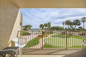 Un balcón con vistas a un campo de golf, palmeras y un edificio al fondo.