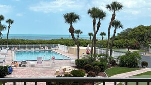 A pool area with a fenced swimming pool, lounge chairs, and palm trees. - Oceanfront Balcony-Private Beach Access-Heated Pool (Cape Canaveral)