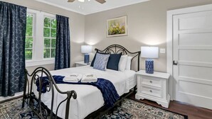 A bedroom with a bed, two bedside tables, a ceiling fan, a window with curtains, and a door. - Blue Bungalow |  2BR 1BA | Lexington (Lexington)