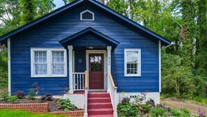A blue house with a red door, white windows, and a brick foundation. - Blue Bungalow |  2BR 1BA | Lexington (Lexington)