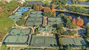 Luchtbeeld van een golfbaan met meerdere tennisbanen, een vijver en omliggend groen.