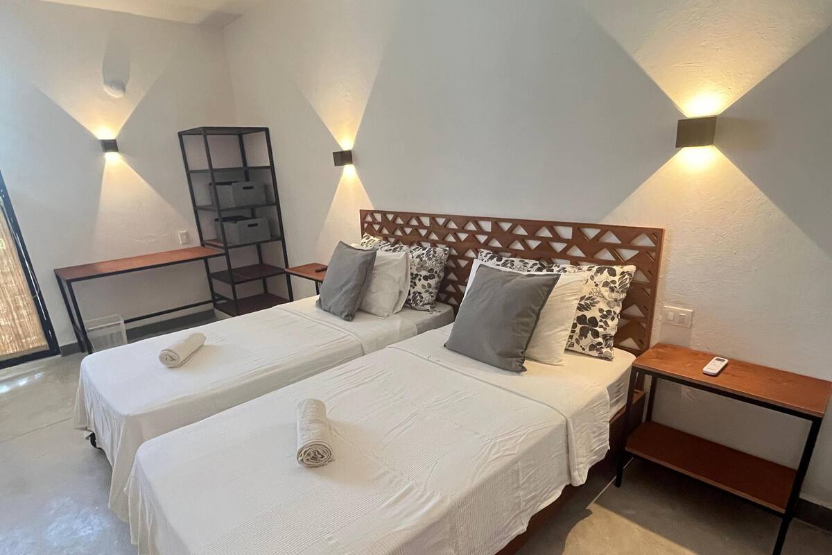 A hotel room with two beds, a wooden headboard, bedside tables, and wall-mounted lighting.