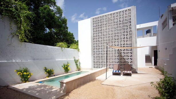 A modern outdoor area with a pool, seating, and a white wall with a lattice design. - Casa Lluavi (Mérida)