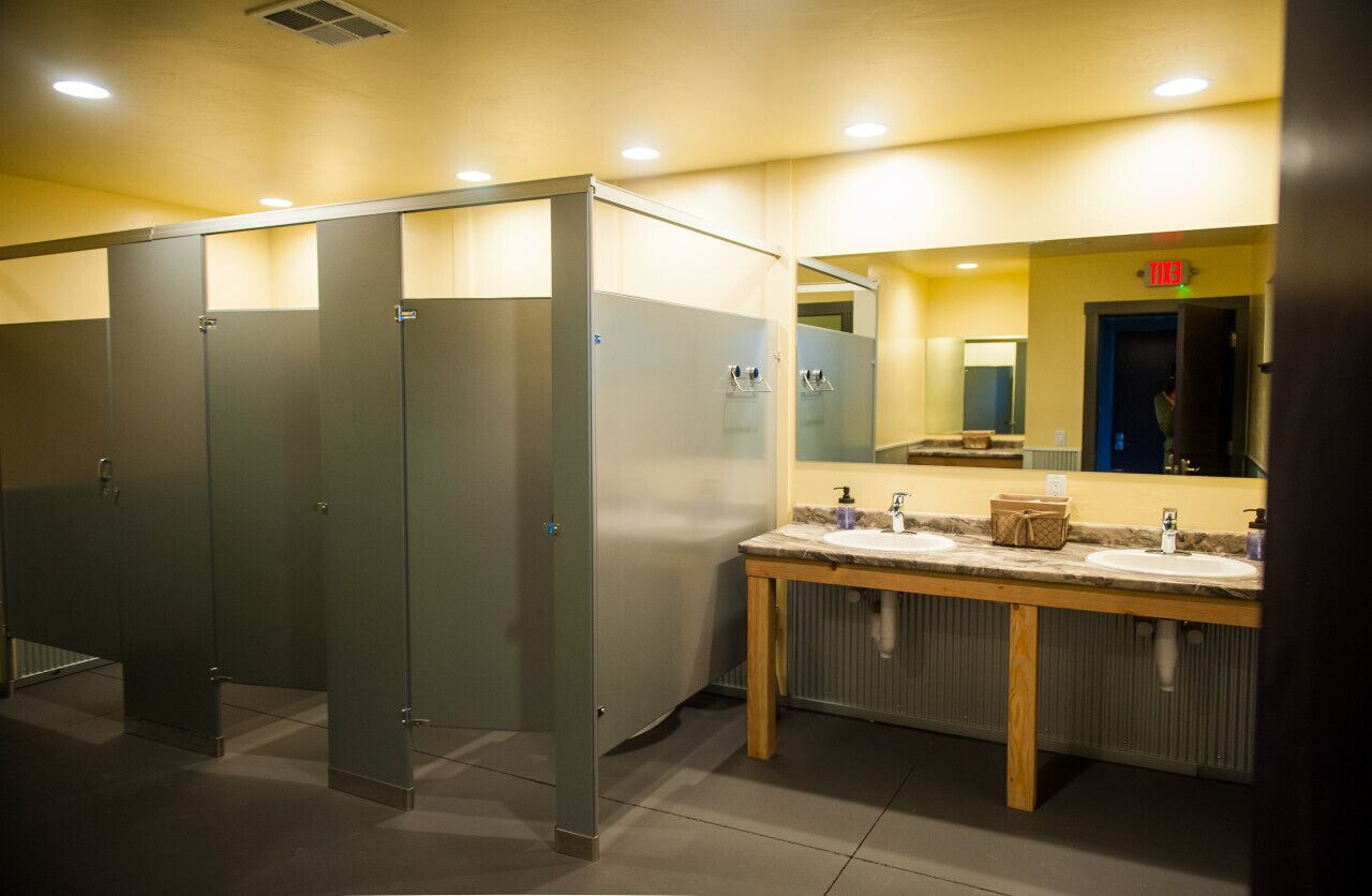 A public restroom with multiple stalls, a vanity with sinks, and a mirror.