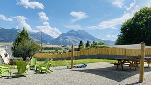 Un espace extérieur aménagé avec des tables de pique-nique et des chaises vertes, une clôture en bois et une vue sur les montagnes en arrière-plan.