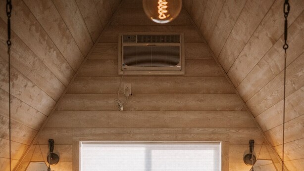 Une chambre mansardée chaleureuse, avec un plafond en pente, une grande fenêtre et un lit avec deux oreillers.