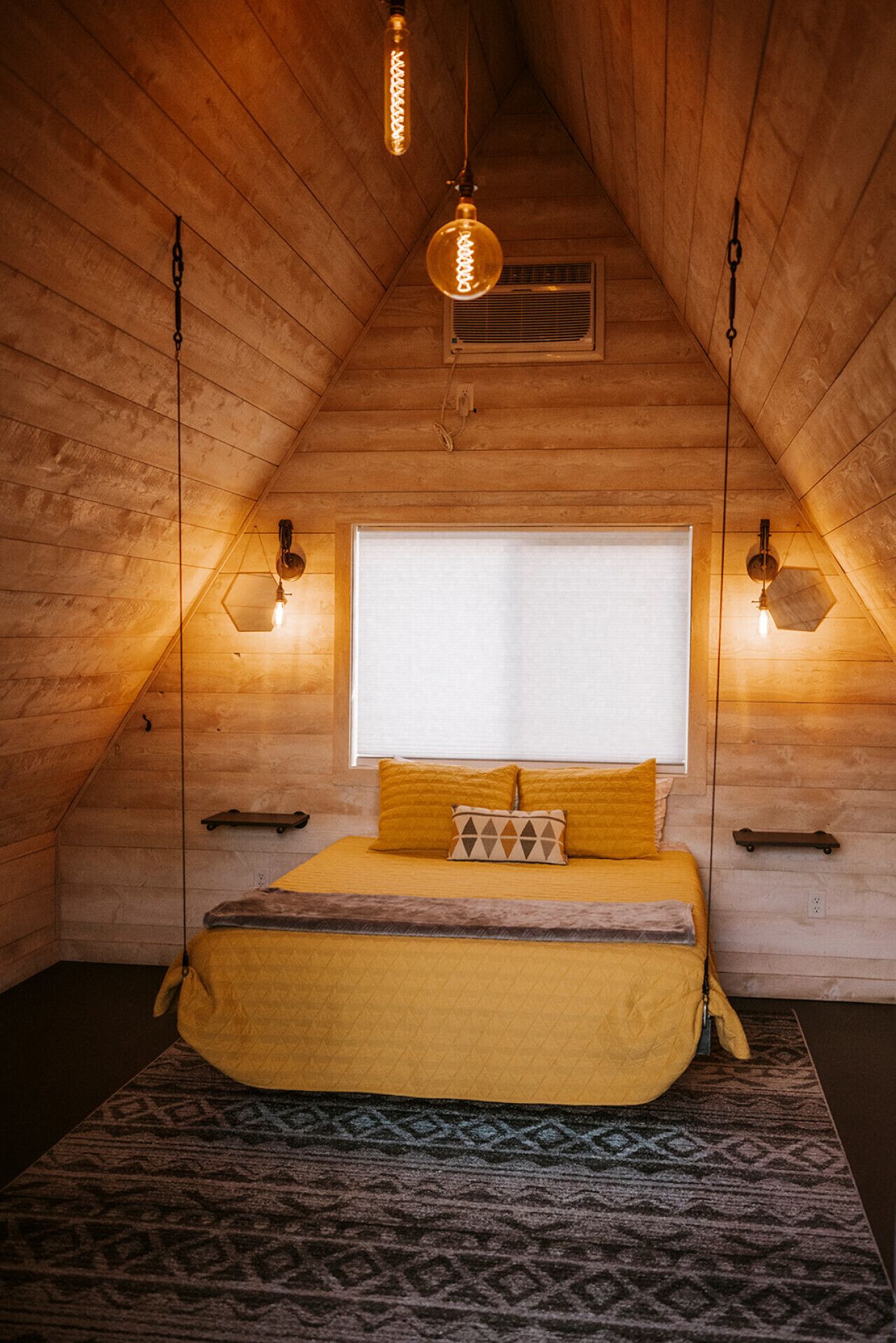 Een gezellig slaapkamer op zolder met een bed, een raam en hanglampen.