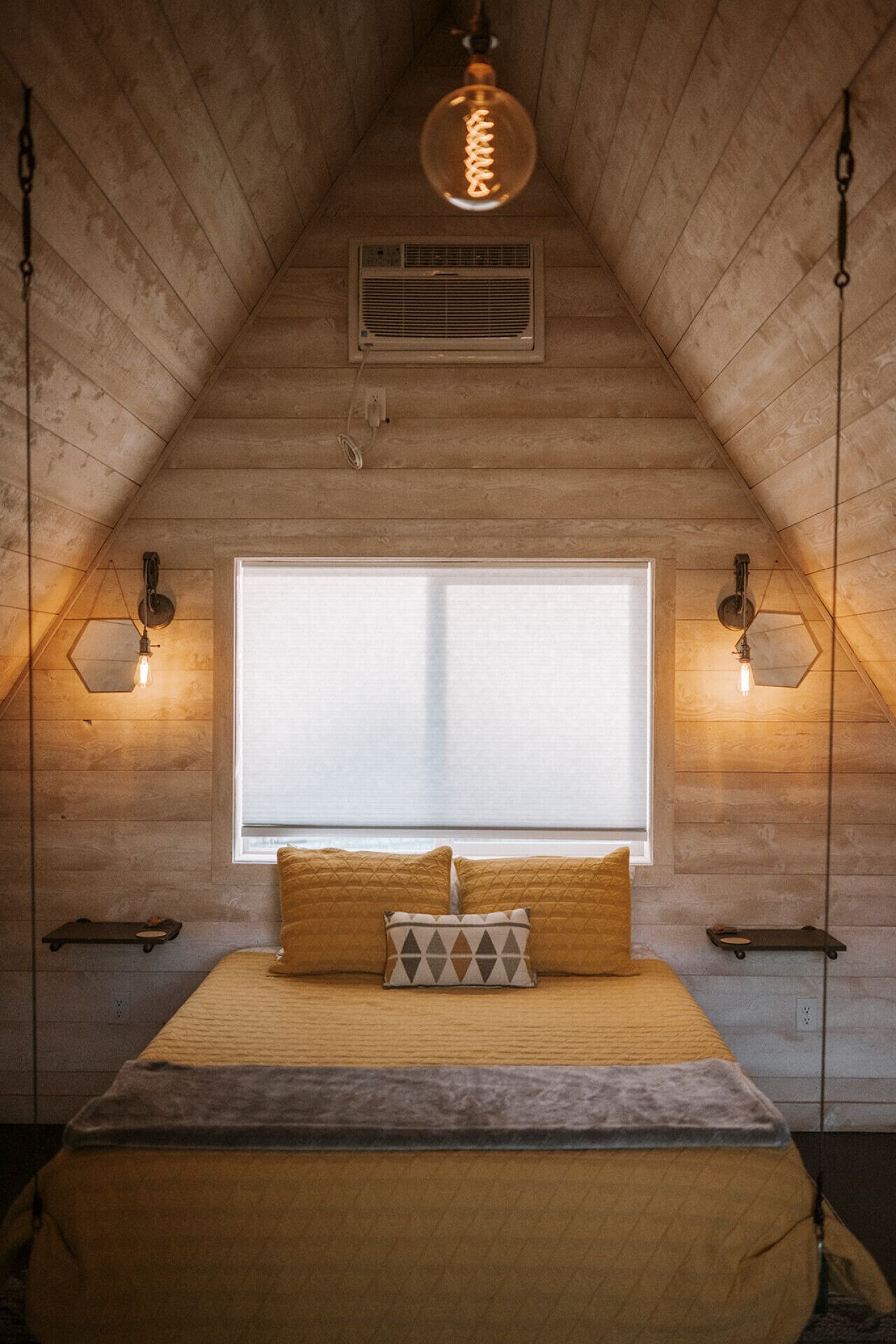 A cozy attic bedroom with a sloped ceiling, a large window, and a bed with two pillows.