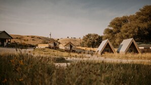 A campsite with several wooden tents and a small building, surrounded by grassy fields and trees.