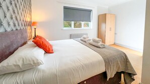 Una cama bien hecha con almohadas, una lámpara de noche y una ventana con persianas.