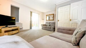 Amplia sala de estar con un televisor de pantalla plana grande, un sofá, un sillón y una puerta que da a otra habitación.
