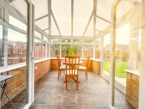A conservatory with a brick wall, a tiled floor, and a table with chairs. - Rider Gardens Holiday Home (Boston)