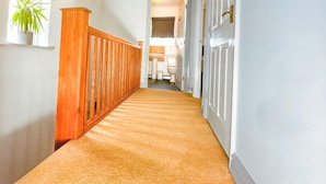 Un pasillo con barandilla de madera, piso alfombrado y paredes blancas.