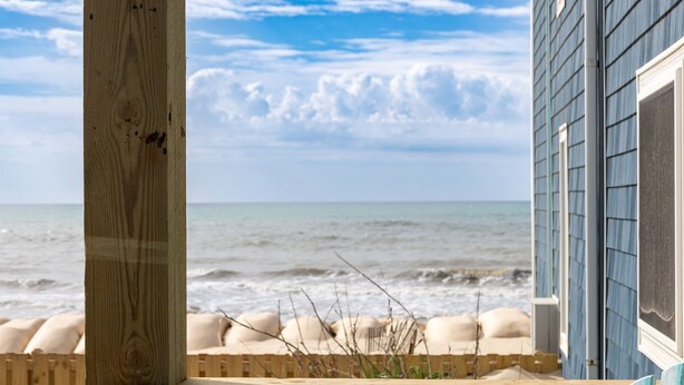 Een houten terras met uitzicht op de oceaan en een gebouw met blauwe bekleding.