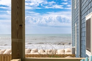 Une terrasse en bois offrant une vue sur l’océan et un bâtiment dont le revêtement extérieur est bleu.