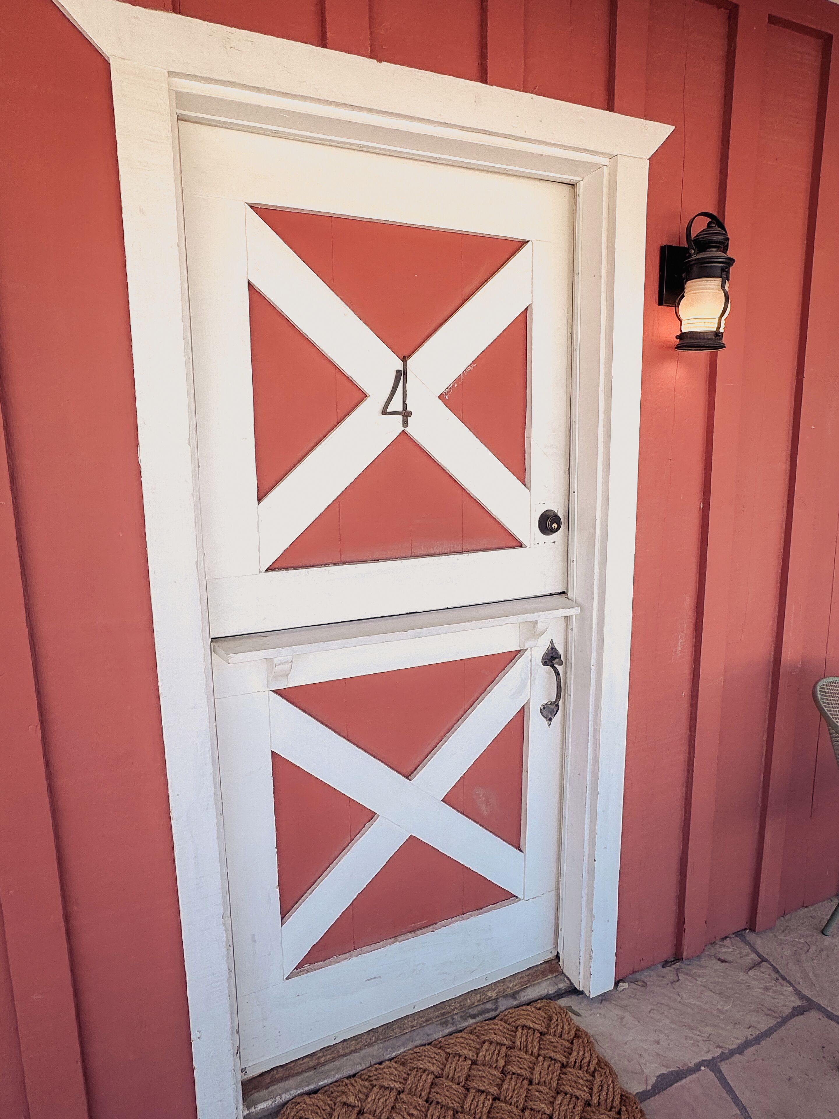 A white double door with a number '4' on it, set in a red building with a doormat and a wall-mounted light fixture.