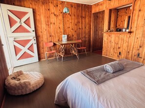 Una habitación acogedora con cama, una mesa de madera con sillas, un sillón mullido y un armario de madera.