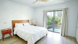 Ein Schlafzimmer mit einem großen Bett, einem Holz-Kopfende, einem Nachttisch, einem Deckenventilator und Blick auf einen Swimmingpool durch eine Glastür.