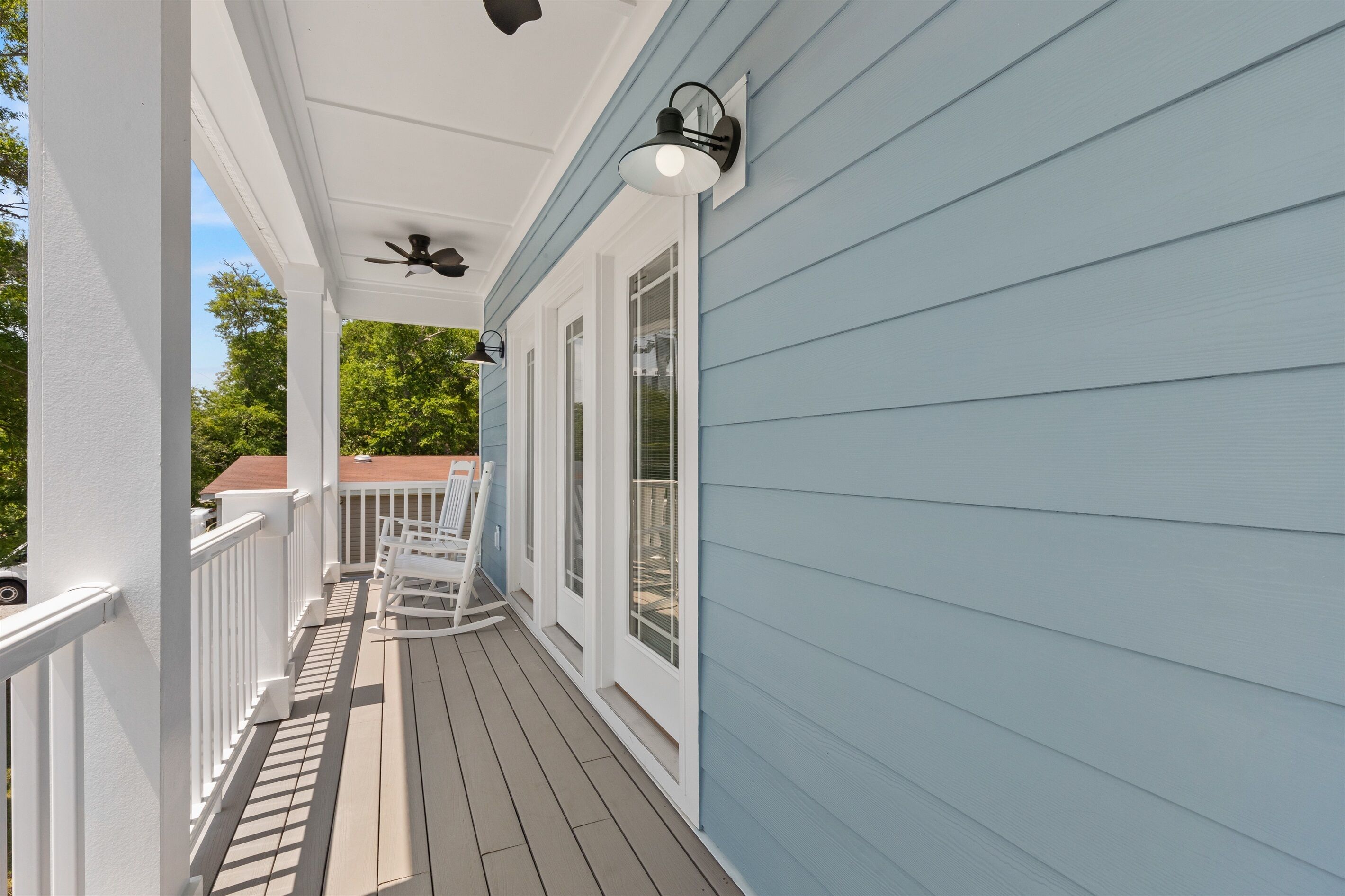 Une véranda couverte avec des balustrades blanches, un ventilateur de plafond et un luminaire.