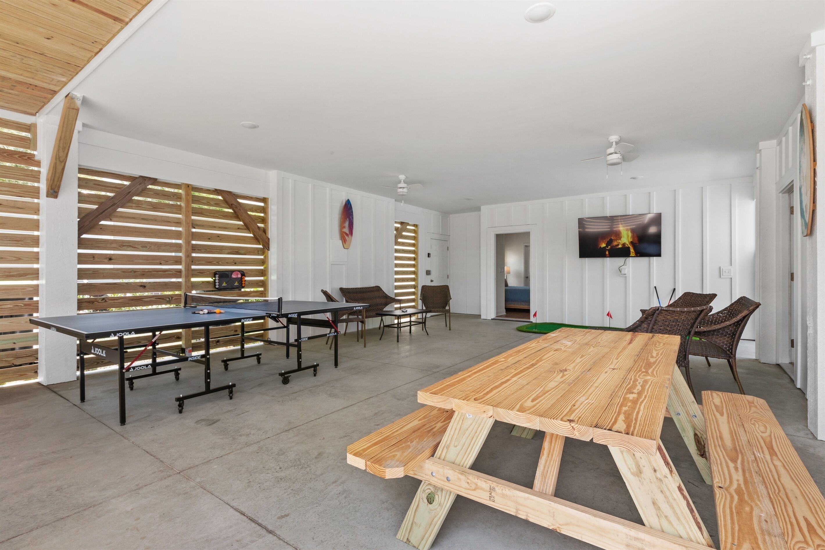 A spacious room with a ping pong table, seating area, and a TV mounted on the wall.