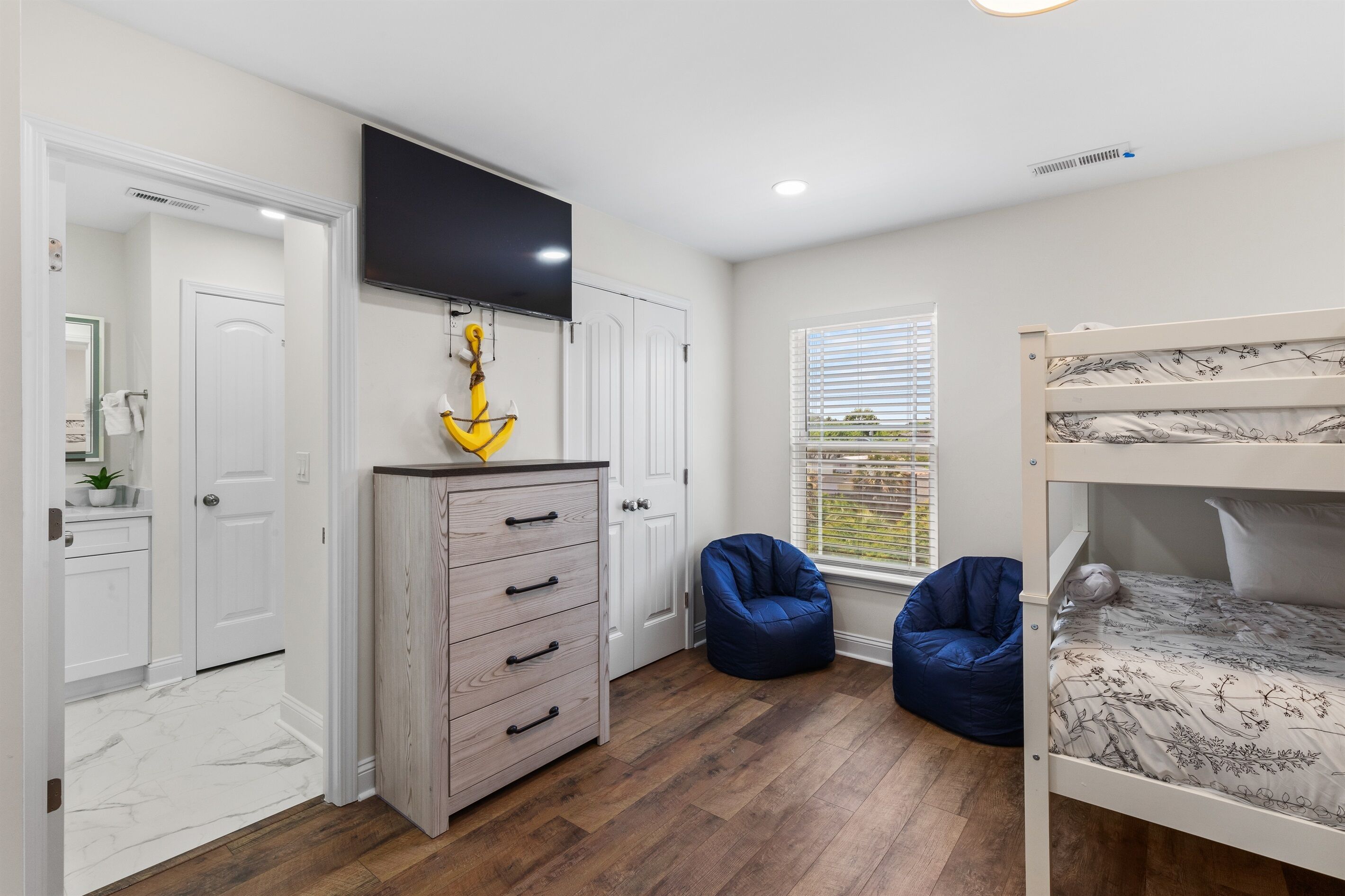 A bedroom with a bunk bed, a dresser, a television, and a window with blinds.