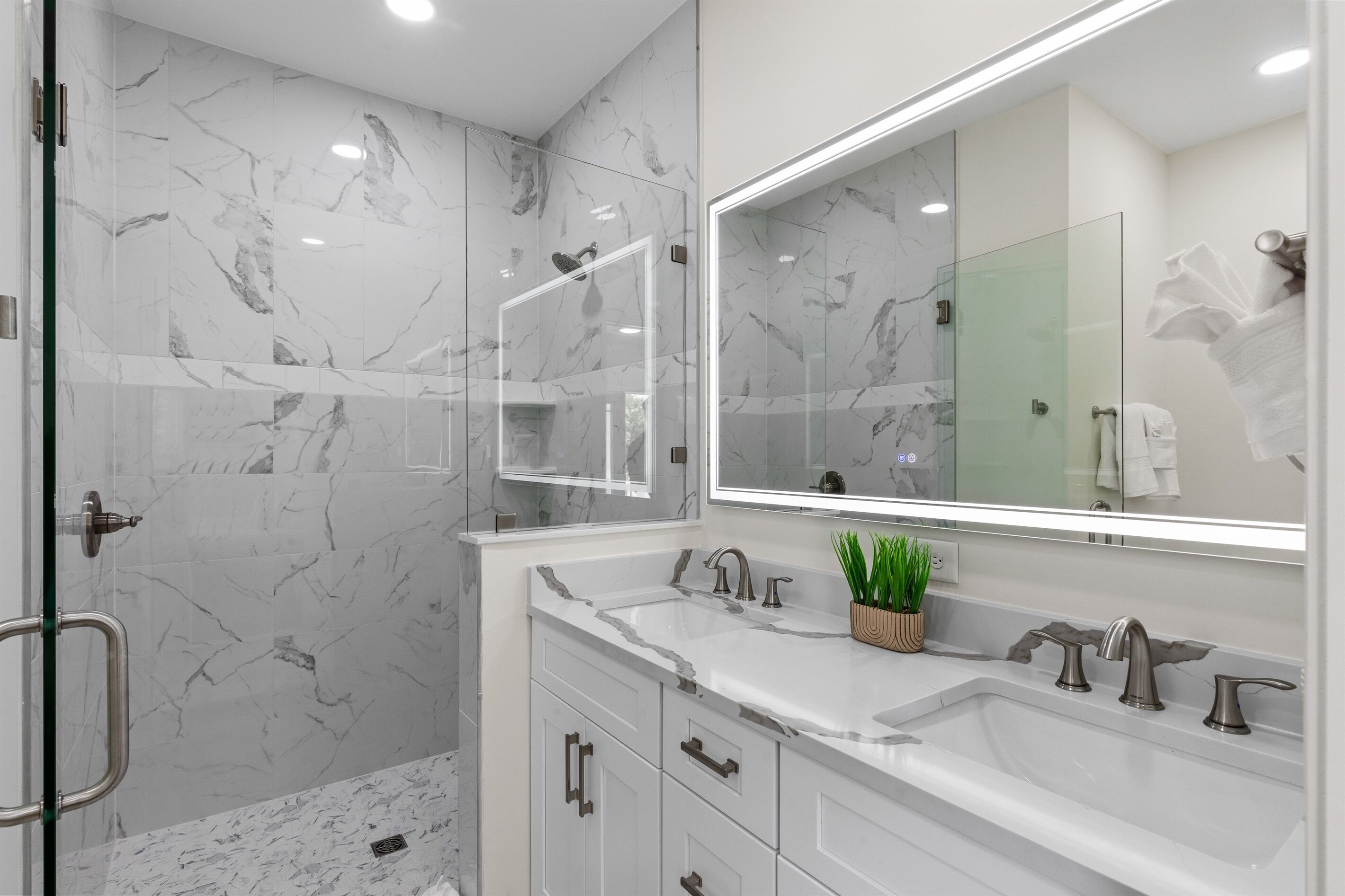 A modern bathroom with marble walls, a glass shower enclosure, and a vanity with a mirror and two sinks.