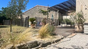Ein Patio mit Pergola, Sitzgelegenheiten im Freien und einem dahinterliegenden Steinhaus.